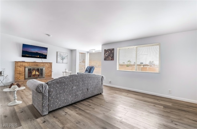 living room featuring a brick fireplace, baseboards, and wood finished floors