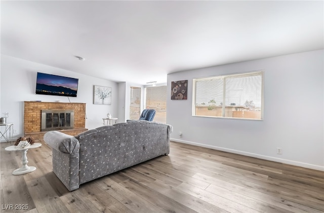 living room featuring a brick fireplace, baseboards, and wood finished floors