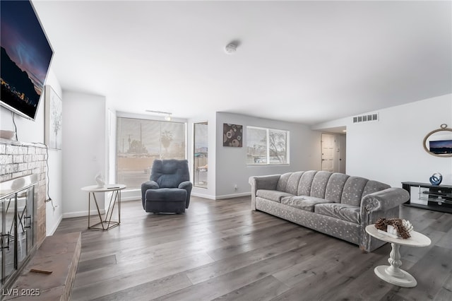 living room featuring a brick fireplace, visible vents, baseboards, and wood finished floors