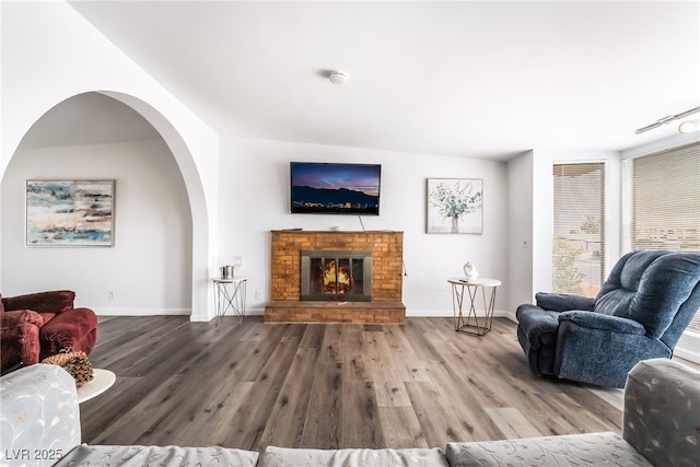 living room with a brick fireplace, baseboards, and wood finished floors