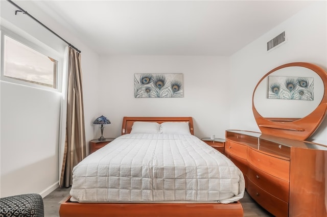 bedroom with baseboards, visible vents, and wood finished floors