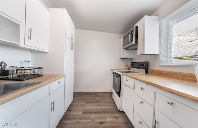 kitchen featuring white electric stove, baseboards, stainless steel microwave, wood finished floors, and white cabinetry