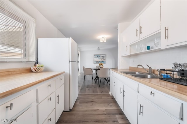 kitchen with light countertops, freestanding refrigerator, white cabinets, a sink, and wood finished floors