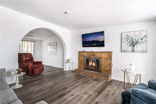 living area with a brick fireplace, baseboards, arched walkways, and wood finished floors