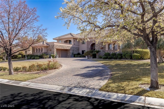 mediterranean / spanish-style house featuring a balcony, stone siding, stucco siding, decorative driveway, and a front yard