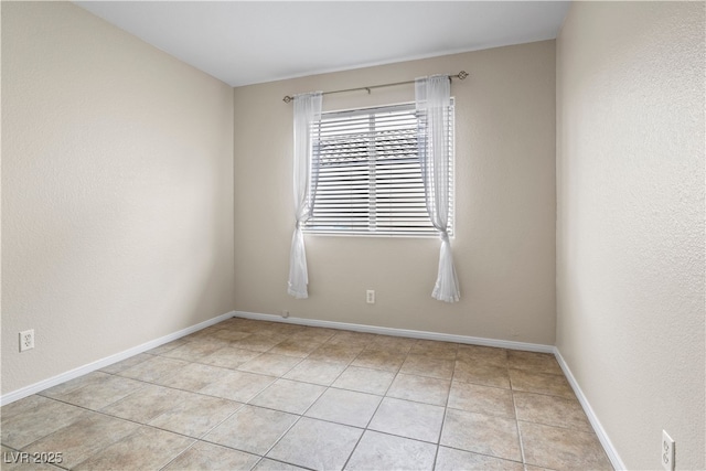 empty room featuring a textured wall, tile patterned flooring, and baseboards