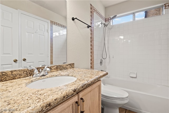 bathroom featuring toilet, a textured wall, vanity, and shower / bathing tub combination