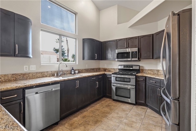 kitchen featuring appliances with stainless steel finishes, a sink, a towering ceiling, and light stone countertops