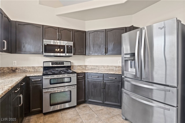 kitchen featuring stainless steel appliances, dark brown cabinetry, light stone counters, and light tile patterned floors