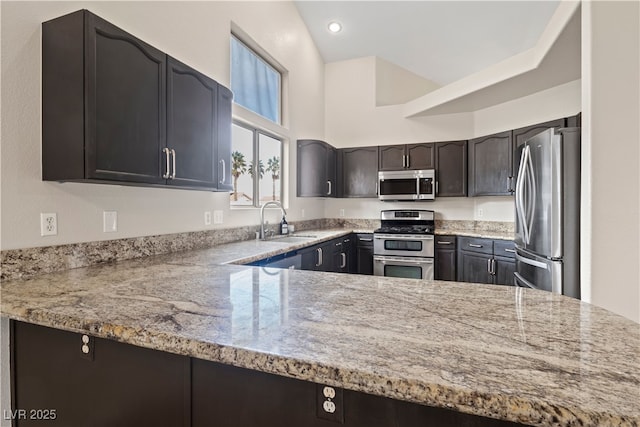 kitchen with stainless steel appliances, recessed lighting, a sink, light stone countertops, and a peninsula