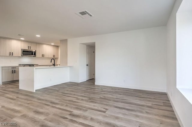 kitchen with light wood-style flooring, a sink, visible vents, baseboards, and stainless steel microwave