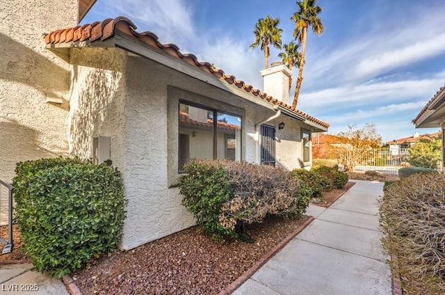 view of property exterior with fence, a tile roof, and stucco siding