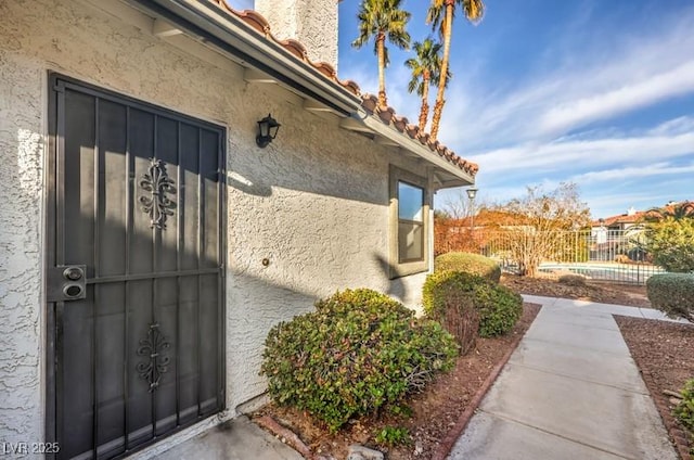 exterior space featuring fence, a tile roof, and stucco siding