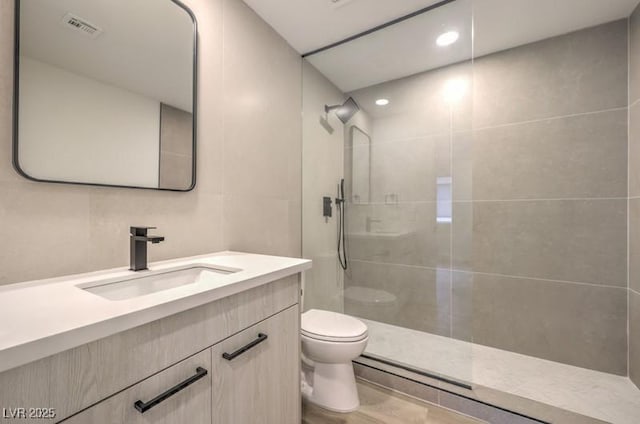 full bath featuring a walk in shower, toilet, visible vents, vanity, and tile walls