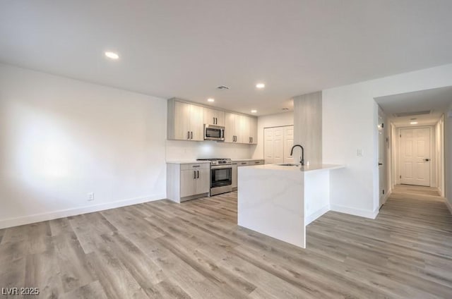 kitchen with stainless steel appliances, a sink, light countertops, and light wood-style floors