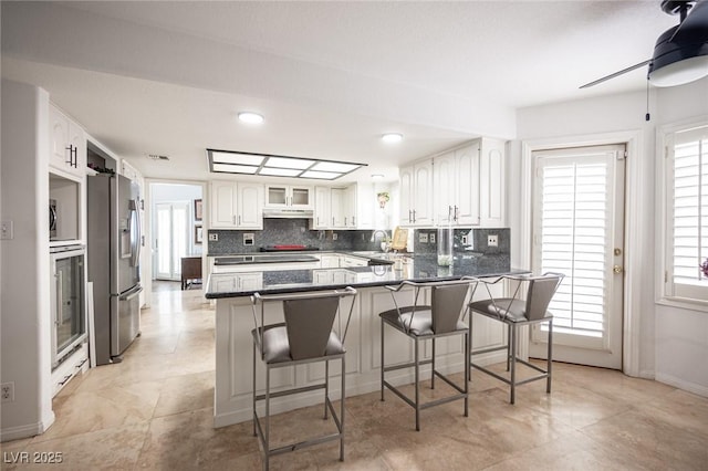 kitchen with tasteful backsplash, appliances with stainless steel finishes, white cabinetry, a peninsula, and a kitchen bar