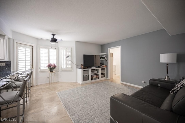 living area with a ceiling fan and baseboards