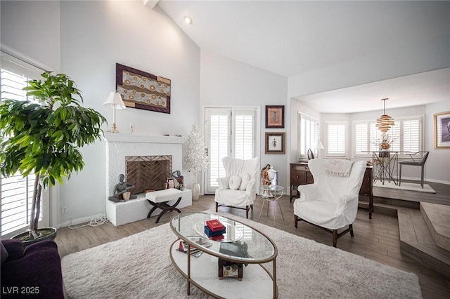 living area with baseboards, high vaulted ceiling, a fireplace with raised hearth, and wood finished floors