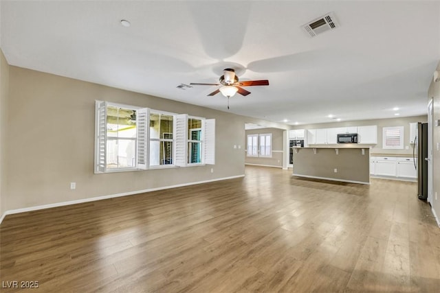 unfurnished living room with baseboards, wood finished floors, visible vents, and a ceiling fan