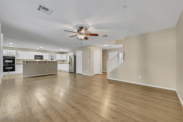 unfurnished living room with visible vents, stairway, light wood-style flooring, a ceiling fan, and baseboards