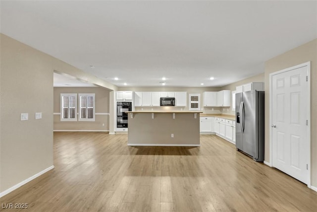 kitchen with open floor plan, white cabinetry, light wood-style flooring, and black appliances