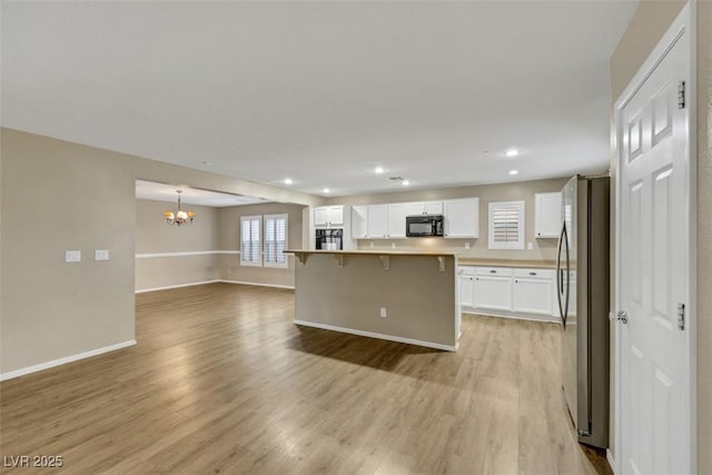 kitchen with freestanding refrigerator, open floor plan, light wood-type flooring, black microwave, and a kitchen bar