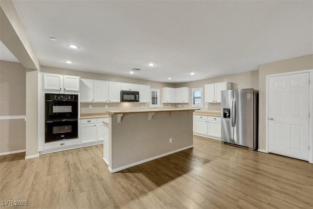 kitchen with black appliances, light wood finished floors, a breakfast bar area, and white cabinets