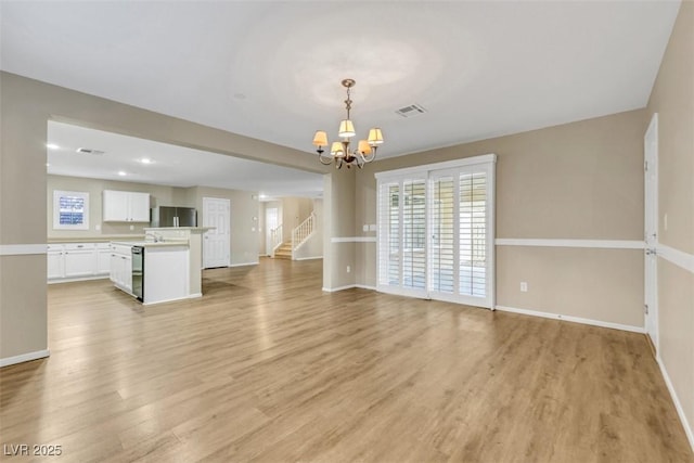 unfurnished living room with a healthy amount of sunlight, visible vents, light wood finished floors, and an inviting chandelier