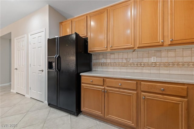 kitchen featuring brown cabinets, tasteful backsplash, light countertops, light tile patterned flooring, and black fridge