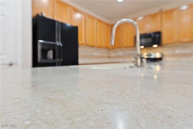 kitchen featuring light brown cabinetry, speckled floor, a sink, and black fridge