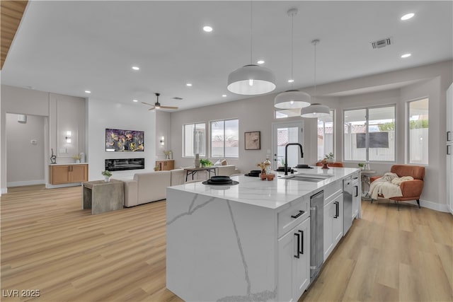 kitchen with a glass covered fireplace, open floor plan, white cabinetry, and a sink