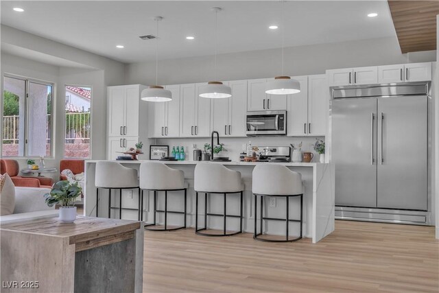 kitchen with light wood finished floors, a breakfast bar, a kitchen island with sink, white cabinets, and appliances with stainless steel finishes