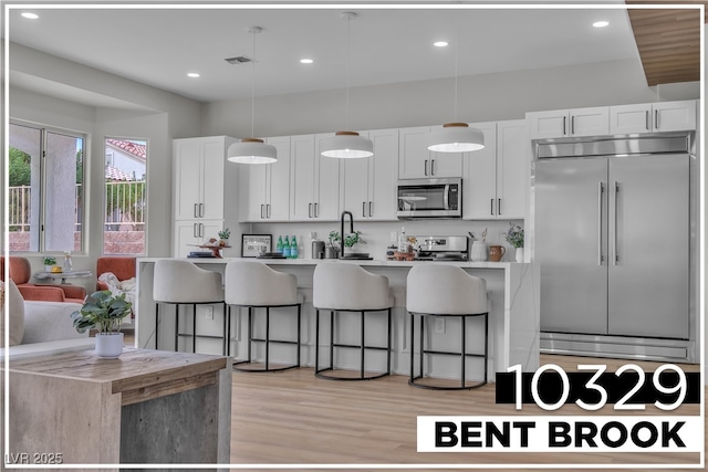 kitchen featuring light wood finished floors, a breakfast bar, a kitchen island with sink, stainless steel appliances, and white cabinets