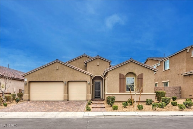 mediterranean / spanish home with decorative driveway, an attached garage, a tile roof, and stucco siding