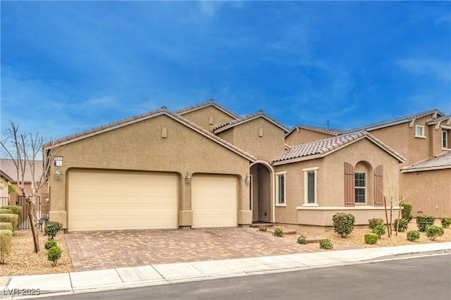 mediterranean / spanish house featuring decorative driveway, a tile roof, an attached garage, and stucco siding