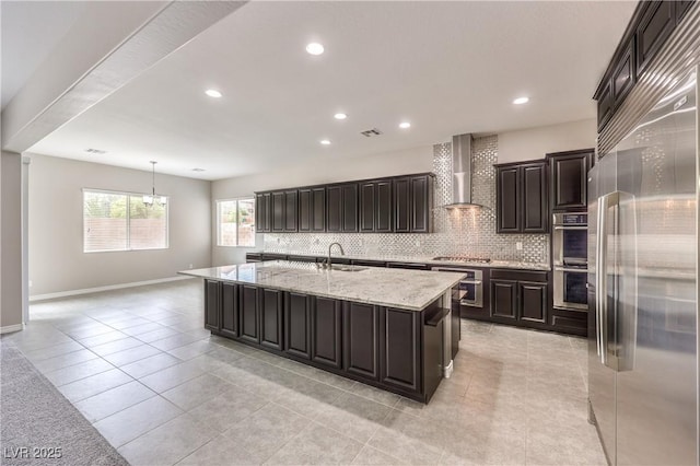 kitchen featuring stainless steel appliances, wall chimney range hood, a sink, and decorative backsplash