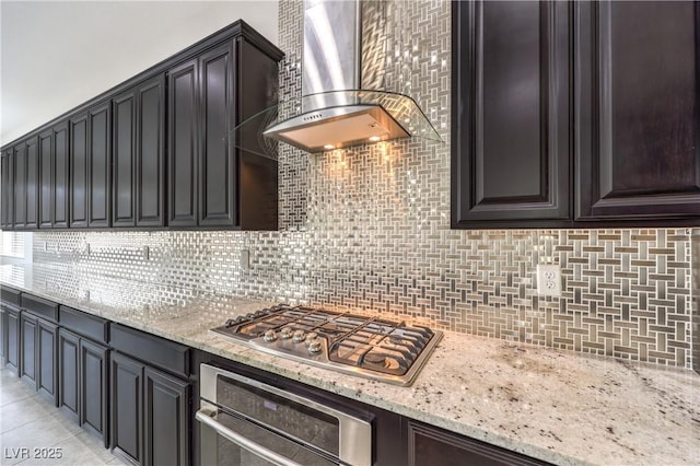 kitchen featuring light tile patterned floors, decorative backsplash, light stone counters, stainless steel appliances, and wall chimney range hood