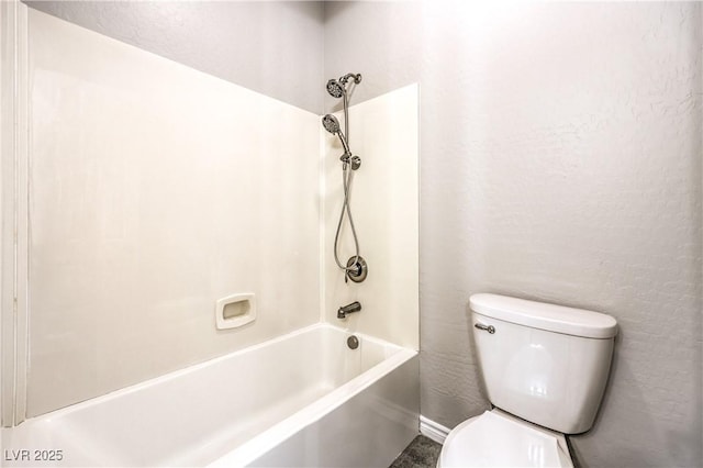 bathroom with shower / washtub combination, a textured wall, and toilet