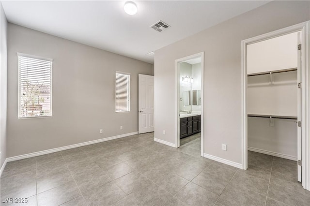 unfurnished bedroom with a walk in closet, visible vents, baseboards, and ensuite bathroom