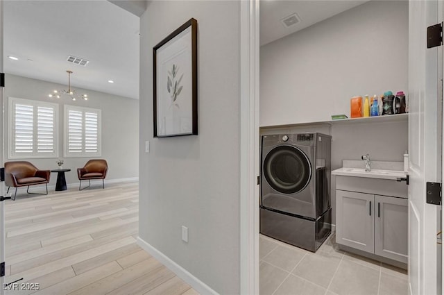 laundry area with light wood-style flooring, laundry area, a sink, visible vents, and washer / dryer