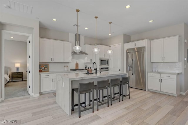 kitchen featuring a breakfast bar, stainless steel appliances, wall chimney range hood, white cabinetry, and a sink