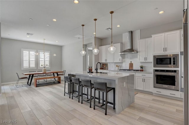 kitchen with decorative backsplash, wall chimney exhaust hood, appliances with stainless steel finishes, light wood-type flooring, and a sink