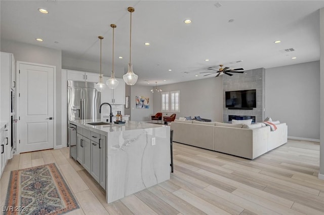 kitchen with light wood finished floors, recessed lighting, a kitchen island with sink, a sink, and light stone countertops