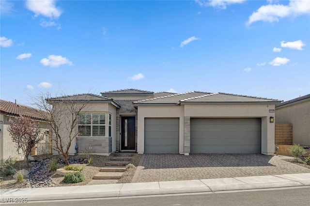 prairie-style house with decorative driveway, a tile roof, an attached garage, and stucco siding