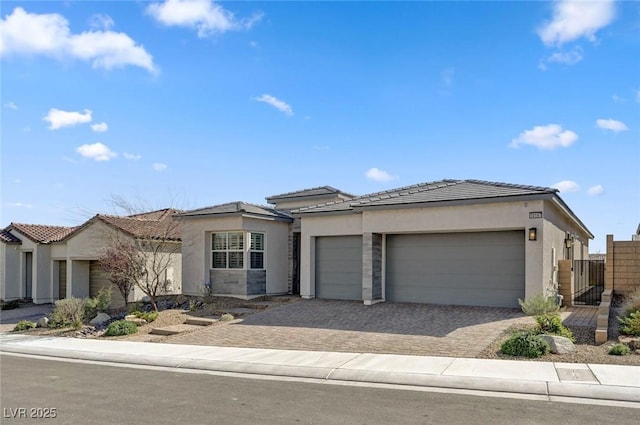 view of front of house featuring a tiled roof, an attached garage, fence, decorative driveway, and stucco siding