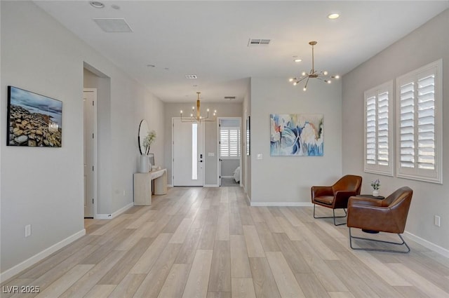 foyer entrance featuring baseboards, light wood-style floors, visible vents, and an inviting chandelier