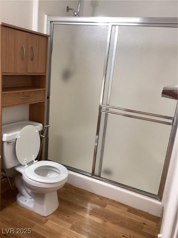 bathroom with a stall shower, wood finished floors, and toilet