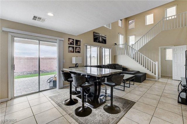 dining area featuring visible vents, baseboards, stairs, light tile patterned floors, and a towering ceiling