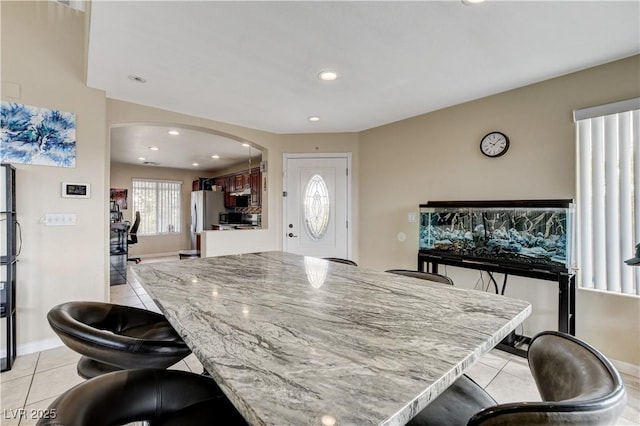 kitchen featuring arched walkways, light tile patterned floors, a breakfast bar area, and freestanding refrigerator