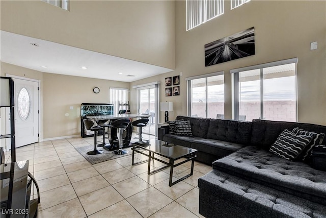 living area with light tile patterned floors, baseboards, a towering ceiling, and recessed lighting